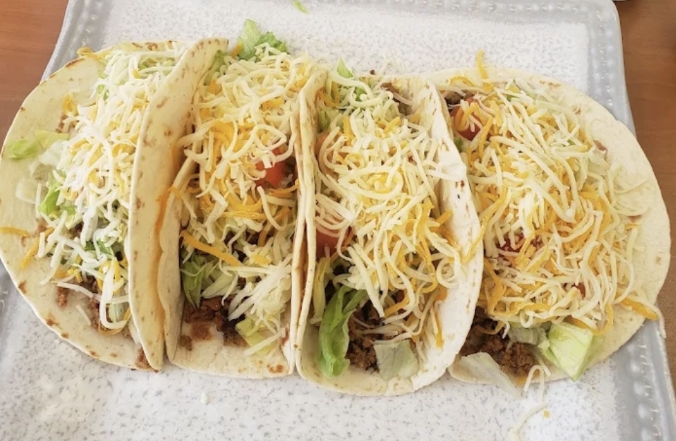 Four American tacos topped with shredded cheese, lettuce and tomato